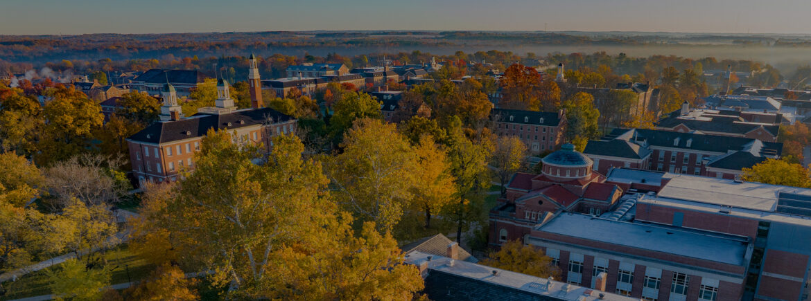 Aerial panoramic view of the Miami Oxford campus with red brick buildings surrounded by bright autumn foliage under a clear sky.
